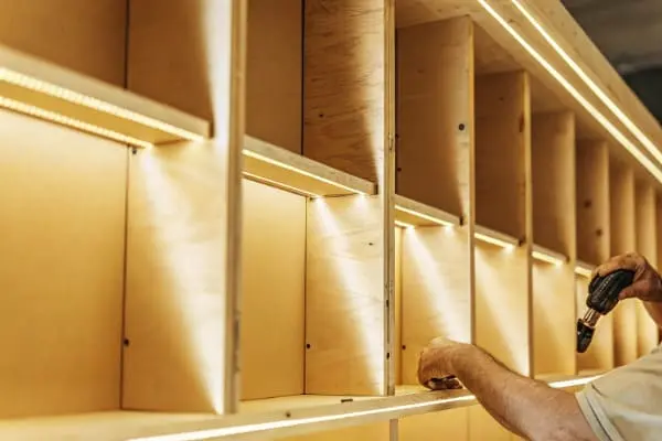 Contractor quickly installing photorealistic LED strip lighting into custom wooden shelving units (ID#3)